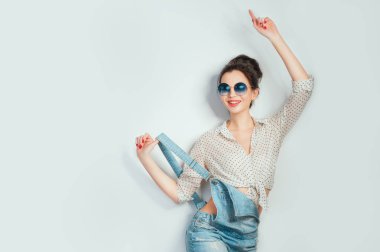 Sıcak gün! Güzel neşeli olan kadın saç topuz güneş gözlüğü dans ve beyaz duvardan poz kot şort giyiyor. İyi bir ruh hali. İnsanların duyguları güzellik moda yaşam tarzı kavramları