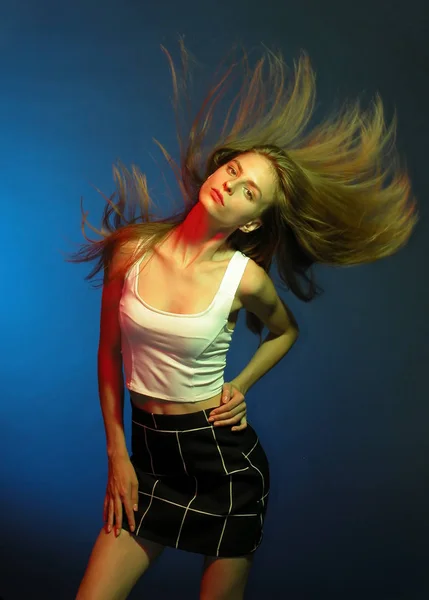 Colored light. Young girl shakes her head with long hair on blue background.