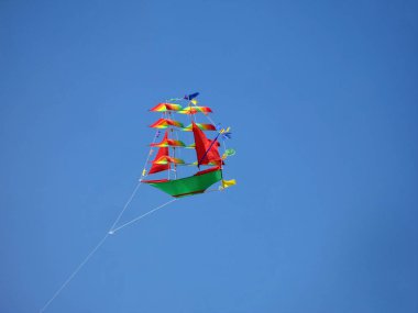 Children kite in the form of multicolored ship  flying on sky background. clipart