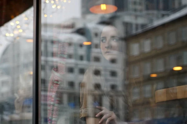 Una chica con problemas se sienta detrás de la ventana del café — Foto de Stock