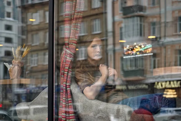 Una chica triste se sienta detrás de una ventana de la cafetería — Foto de Stock