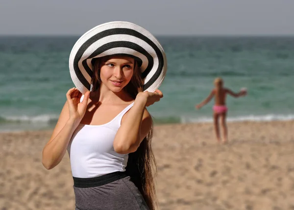 Mulher bonita em t-shirt branca e chapéu de brimmed na praia — Fotografia de Stock