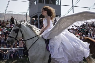 Onun arkasından büyük kanatları ile uzun saçlı kız beyaz ata biniyor