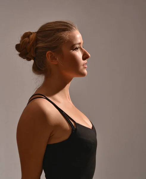 Half-length profile of young girl in black T-shirt with open shoulders posing in studio on grey. — Stock Photo, Image