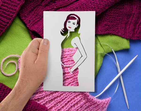 Uma mão segura um estêncil de papel de uma jovem de cabelos compridos contra o fundo de agulhas de tricô e fios de lã — Fotografia de Stock
