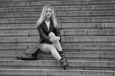 Bir kot etek ve siyah bir ceket şehrin güzel bir kadın. Işık saç, beyaz bir bluz örme. Siyah çanta.