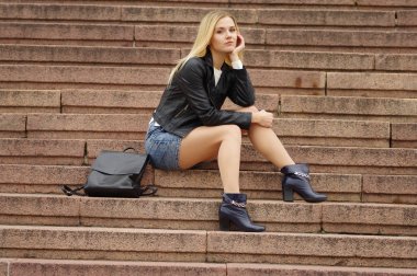 Siyah ceketli güzel bir kız merdivende oturuyor.