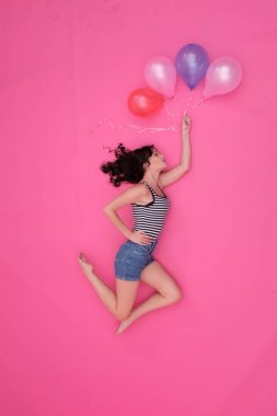 Ulusal teketim ürünleri üzerinde pembe bir arka plan üzerinde uçan bir siyah saçlı kız.