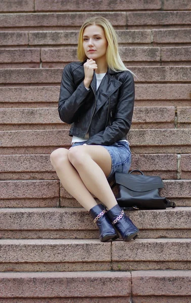 Una hermosa chica con una chaqueta negra está sentada en las escaleras — Foto de Stock