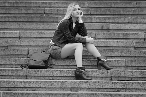 Una bella ragazza con una giacca nera è seduta sulle scale . — Foto Stock