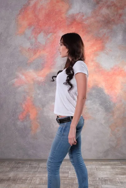 Mooie brunette vrouw in jeans en een wit T-shirt, permanent in een sexy pose. — Stockfoto