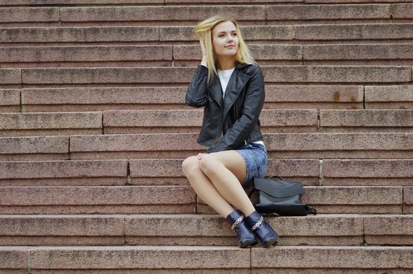 Una hermosa chica con una chaqueta negra está sentada en las escaleras — Foto de Stock