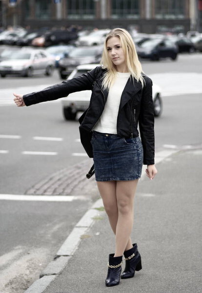 Красивая блондинка пытается подцепить машину на дороге.
.