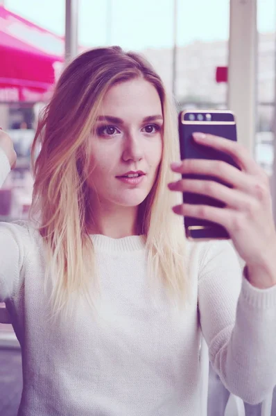 Portrét blondýna v bílém svetru, takže selfie smartphone. — Stock fotografie