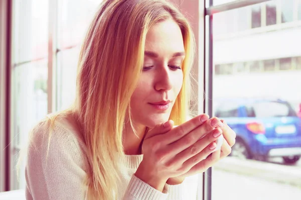 Retrato de una rubia en suéter blanco, con una taza de té en las manos . — Foto de Stock