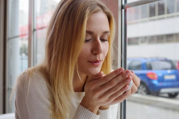 Retrato de una rubia en suéter blanco, con una taza de té en las manos . — Foto de Stock