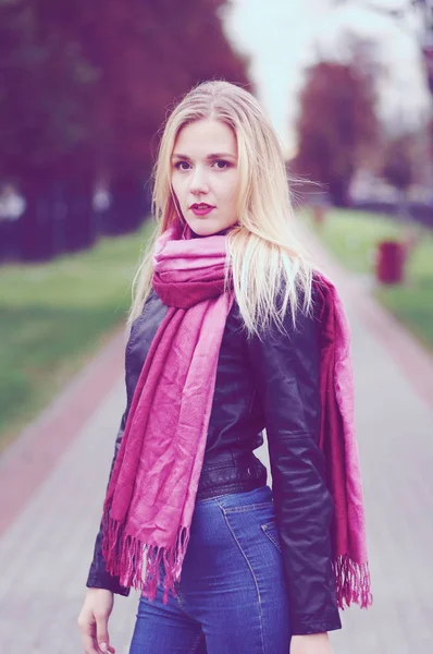 Thoughtful beautiful young woman in leather jacket, blue jeans and red scarf