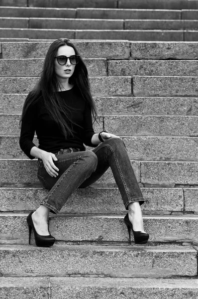Stedelijke portret van een brunette in jeans en een zwart T-shirt met een lange mouwen. Straat mode. — Stockfoto