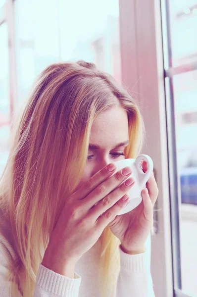 Retrato de una chica en un suéter de punto blanco bebiendo té en un café . — Foto de Stock