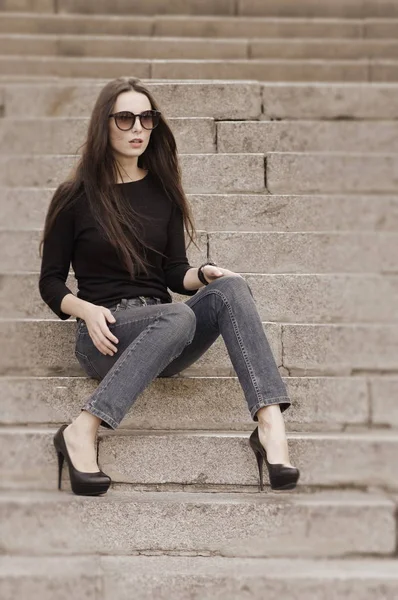 Retrato urbano de una morena en jeans y una camiseta negra con mangas largas. Moda callejera . — Foto de Stock