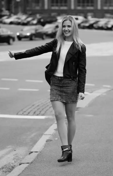 Pretty smiling girl tries to hitch a car on a street. — Stock Photo, Image