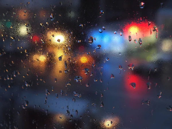 Aurumn rain droplets on window glass with traffic lights.