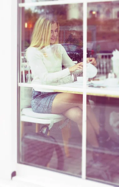 Chica en una falda camisa sentado en un café bebiendo té . — Foto de Stock