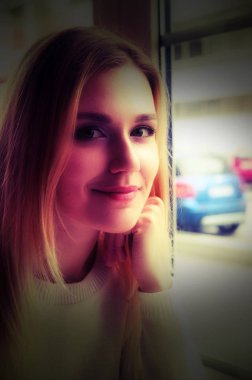 Güzel bir genç kız büyük bir pencere oturmak portre. O yüzündeki nazik bir gülümseme vardır. İçinde belgili tanımlık pencere bulanık araba görüntüdür.