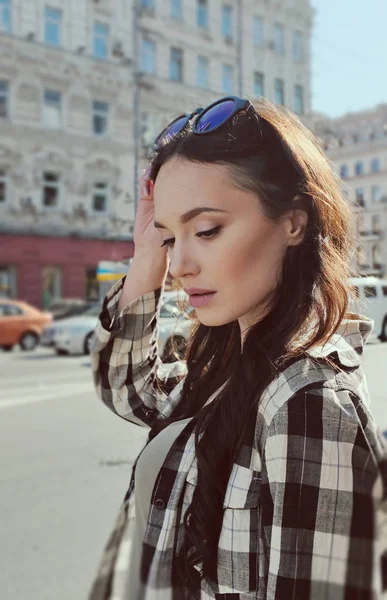 Portrait d'une belle femme brune en chemise à carreaux. Style urbain de vêtements. Lunettes de soleil sur la tête. Reflet du ciel dans les lunettes . — Photo