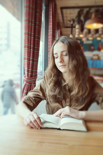 Gadis cantik membaca sebuah buku di sebuah kafe hangat — Stok Foto