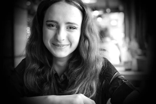 Portret van een lachende langhaar meisje in een bruin blouse. Een meisje zit in een café. Donker bruine ogen, krullend haar. — Stockfoto