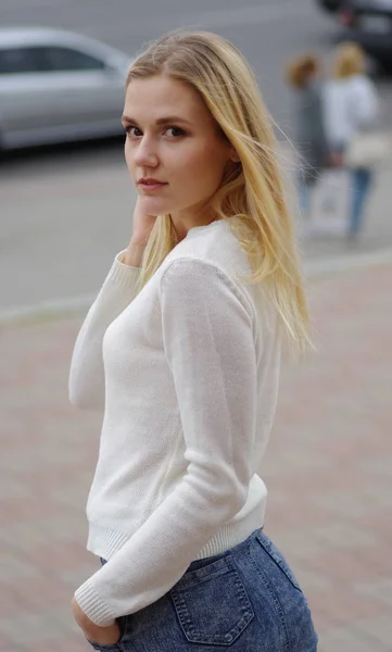 Pretty young woman in white sweater posing in a street — Stock Photo, Image