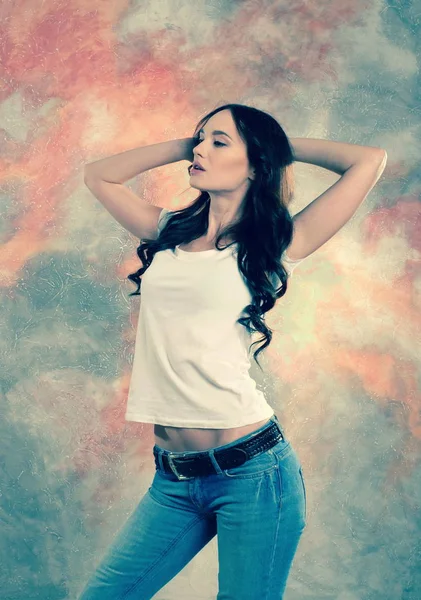Portret van een mooie brunette vrouw in jeans en een witte T-shirt. — Stockfoto