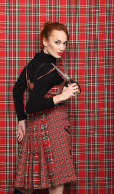 Kırmızı kareli elbiseli, makaslı kızıl saçlı kız.