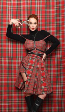 Kırmızı kareli elbiseli, makaslı kızıl saçlı kız.