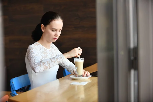 Una donna dai capelli neri in un caffè mescola un latte macchiato — Foto Stock