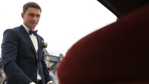 Жених открывает и держит дверь автомобиля для красивой молодой невесты — стоковое видео