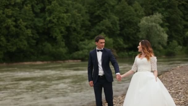 Bruden och brudgummen håller händerna nära floden — Stockvideo