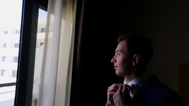 Мужчина выпрямляет галстук у окна — стоковое видео