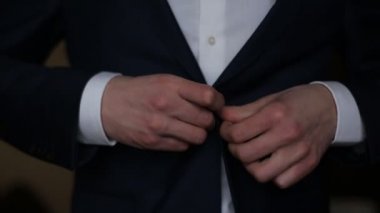 Ceketinin düğmelerini ilikliyorum. Ceketinin düğmelerini bağlayan takım elbiseli şık bir adam dışarı çıkmaya hazırlanıyor. Kapat.