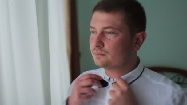 Hombre con camisa blanca atando una corbata cerca de la ventana — Vídeo de stock