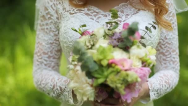 Bonita novia sonriendo a la cámara y oliendo su ramo el día de su boda . — Vídeos de Stock