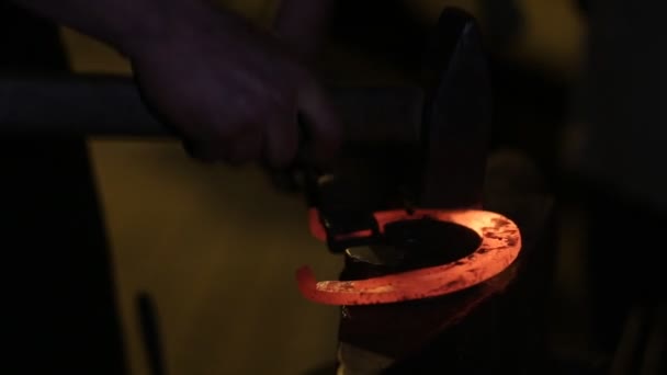 Blacksmith Forges Horseshoe. A blacksmith pounding a hammer on red-hot horseshoe on the anvil. The blacksmith holds a horseshoe steel tongs — Stock Video