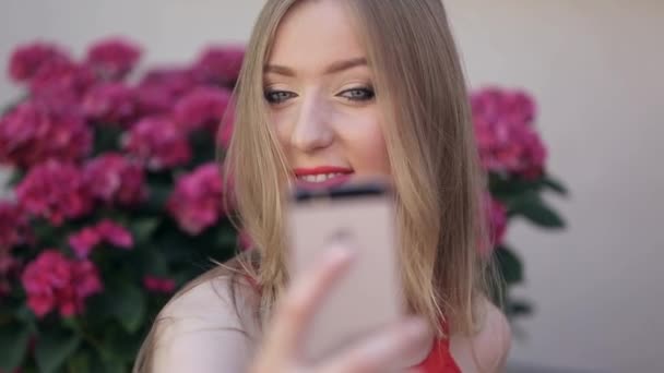 Giovane donna gioca con il suo smartphone, si posa per un selfie, fa un bacio in faccia — Video Stock