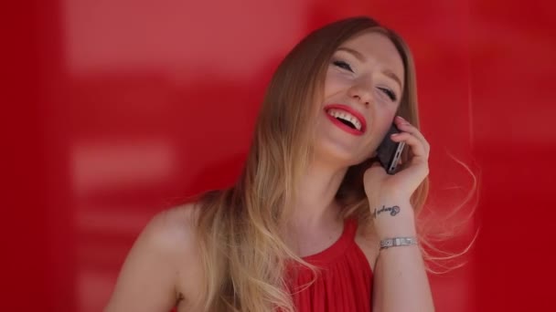 Giovane, sexy, attraente, bella, sorridente donna bionda con lunghi capelli flipping in abito rosso parlare al telefono con qualcuno su sfondo rosso , — Video Stock