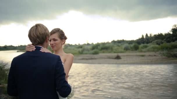 Невеста и жених влюблены на поле возле реки — стоковое видео