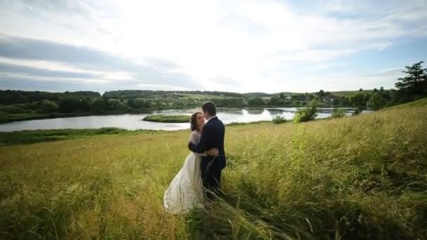 Ο γαμπρός αγκαλιάζει τη νύφη, και στέκονται δίπλα στο ποτάμι — Αρχείο Βίντεο