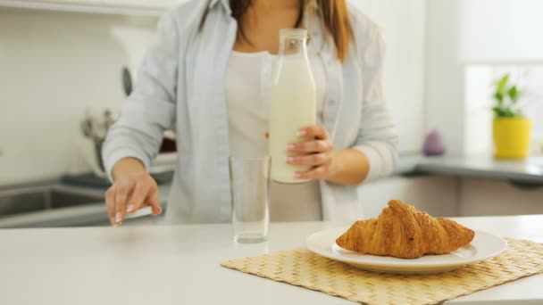 牛奶和羊角面包在桌子上。女人给自己倒杯子里的牛奶. — 图库视频影像