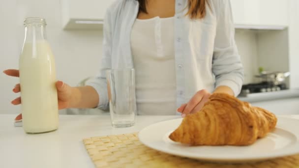 De vrouw in de keuken, gieten zelf melk in het glas. Croissant op tafel. — Stockvideo