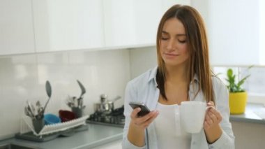 Akıllı telefon kullanan güzel kadın manifatura ve mutfakta kahve içme.